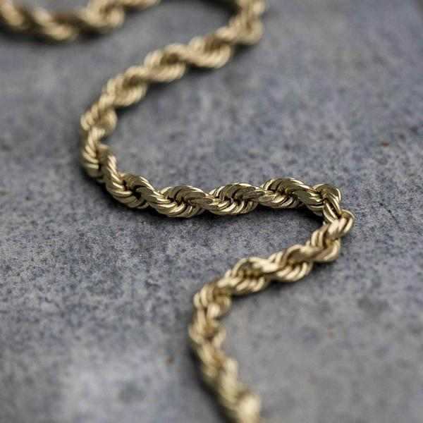 Rope Chain (2mm) in yellow gold laid in an s pattern on top of concrete surface.