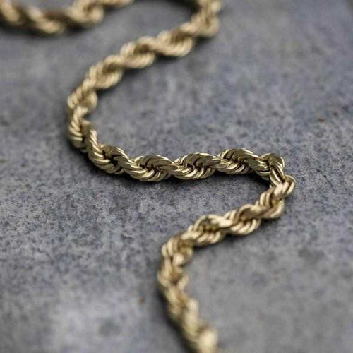 Rope Chain (2mm) in yellow gold laid in an s pattern on top of concrete surface.