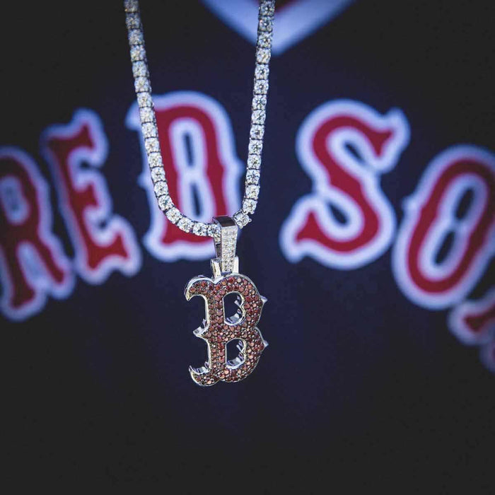 Boston Red Sox MLB Logo Pendant in 14k white gold plating with red gemstones paired with a 3mm Round Cut Tennis Necklace in White Gold, pictured hanging in front of a Red Sox jersey.