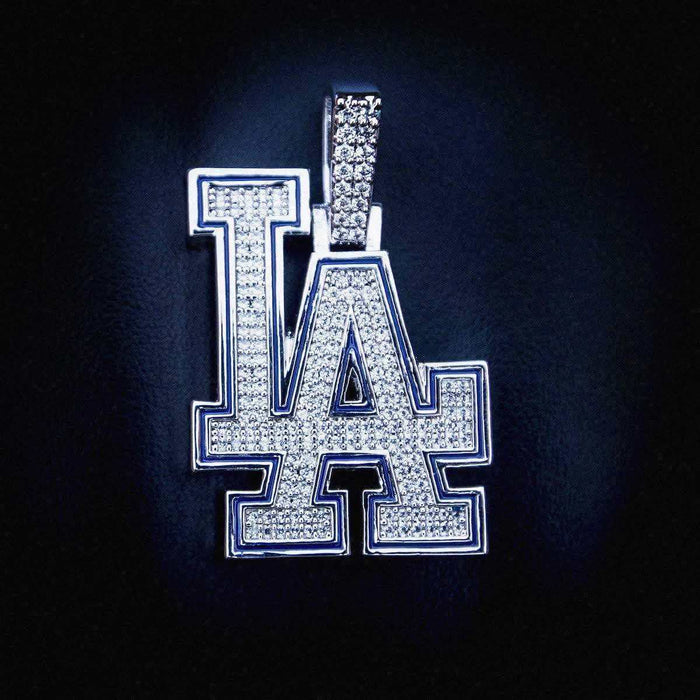 Los Angeles Dodgers MLB Logo Pendant in 14k white gold plating with AAAAA CZ Stones and blue enamel laid flat on a textured surface.