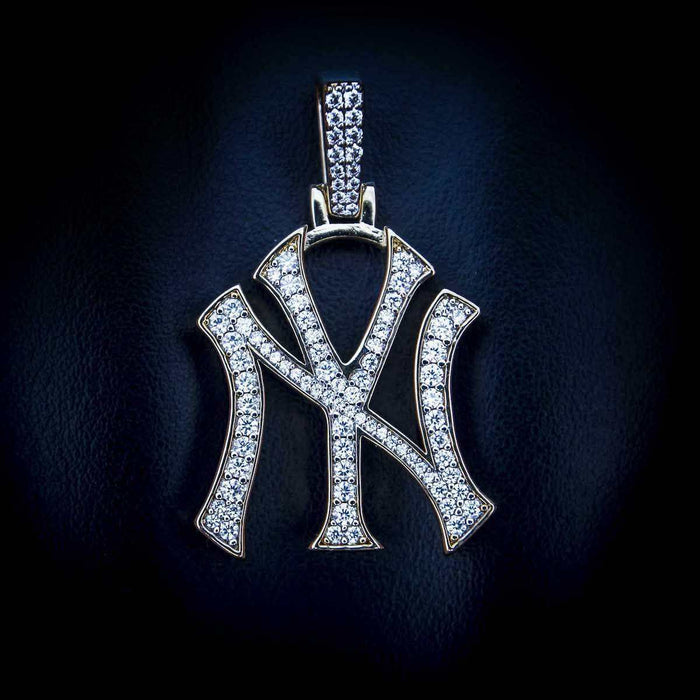 New York Yankees MLB logo pendant in 18k gold plating with CZ Stones laid flat on textured surface.
